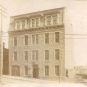 Photographie noir et blanc d’un ancien bâtiment de quatre étages avec des fenêtres donnant sur la rue