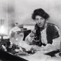 Photographie noir et blanc d’une femme assise à un microscope d’autrefois