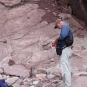Photographie couleur d’un homme debout, bloc-note à la main, devant des rochers roses