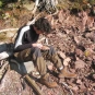 Colour photograph of man sitting on rocky shore with rock in his hand