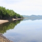 Colour photograph of still water, rocky shoreline and trees
