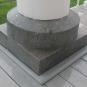 Colour photograph of gray speckled rock carved square at bottom and circular at the top, supporting wooden white column