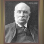 Image noir et blanc d'un homme chauve en complet portant moustache et favoris blancs