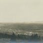 Black and white photograph of town in distance, fields and trees
