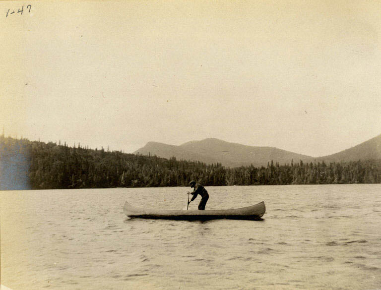Black and white photograph of a man in a canoe with rolling hills in the background