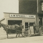 Black and white photograph of a horse and wagon with three men in front of a wooden building