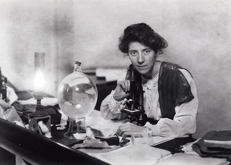 Black and white photograph of a women sitting at a old fashioned microscope